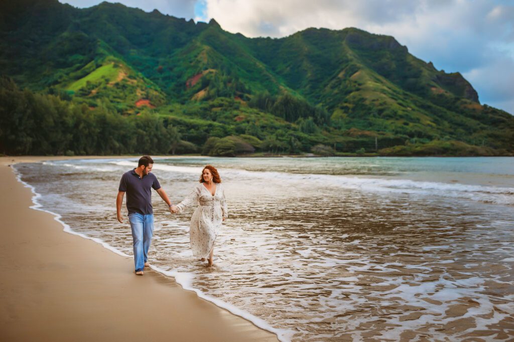 Engaged couple holding hands and walking on Hawaii beach at sunset.
